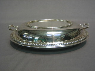 An oval silver plated twin handled entree dish and cover with bead work border