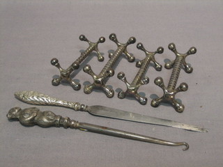 4 polished steel knife rests, a paper knife with silver handle and a silver button hook the handle in the form of a standing bear