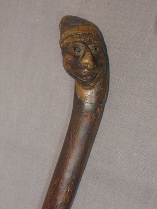 A walking stick, the handle in the form of a stylised head set hardstone eyes, wearing a smoking cap and with silver badge