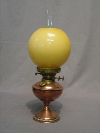 A copper and brass oil lamp with amber shade and clear glass chimney