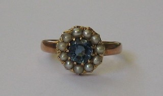 A gold dress ring set a circular cut sapphire supported by demi-pearls