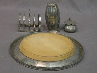 A  circular planished pewter bread board holder, a pewter  5  bar toast rack, ditto sugar castor and mustard pot