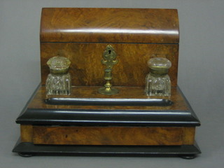 A  Victorian  figured walnut standish, the  back  incorporating  a dome  shaped stationery box, 2 cut glass inkwells, a candle  stick and pen receptical, the base fitted a drawer, by Cormack Bros. of Ludgate Hill 12 1/2"