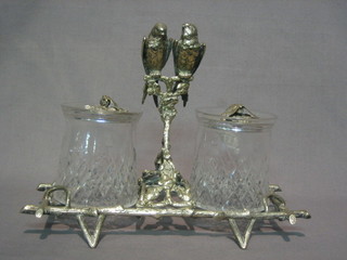 An  Edwardian  silver  plated and cut glass  twin  bottle  preserve stand,  having  2 circular cut glass bottles, the finials in  the  form of  butterflies  (1f) raised on a crab stock stand surmounted  by  2 budgerigars