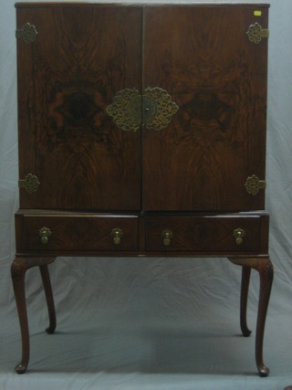 A 1930's Queen Anne style walnut cabinet with shelved interior enclosed by panelled doors, the base fitted 2 drawers raised on cabriole supports 35"