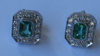 A pair of lozenge cut emerald earrings surrounded by diamonds