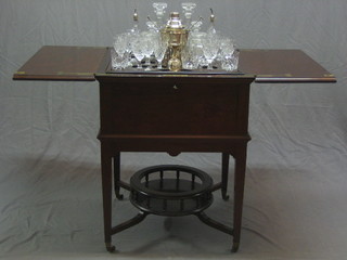 An Edwardian square mahogany surprise table, raised on square tapering supports with circular undertier, fitted a silver plated cocktail shaker, silver plated ice pail, 2 cocktail spoons, a pair of cut glass decanters, a pair of bitters jars, a pair of small cut glass decanters, 2 cut glass pickle jars and a good collection of various cut glass glasses by Harrods 25"