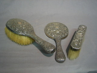 An Eastern 3 piece embossed white metal backed dressing table set with hand mirror, clothes brush and hair brush