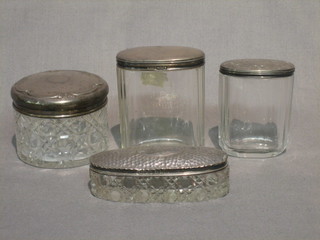 A circular cut glass dressing table jar with embossed silver lid and a shallow oval dressing table jar with silver lid and 2 other dressing table jars with silver lids (4)