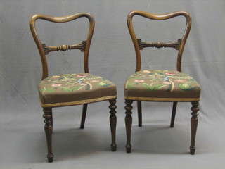 A pair of Victorian rosewood spoon back dining chairs with carved mid rails and upholstered seats, raised on turned supports