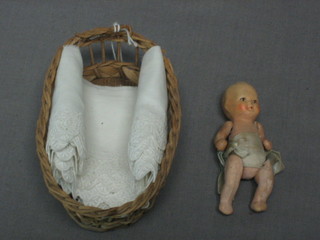 A foreign baby doll with articulated limbs, contained in a basket work cradle