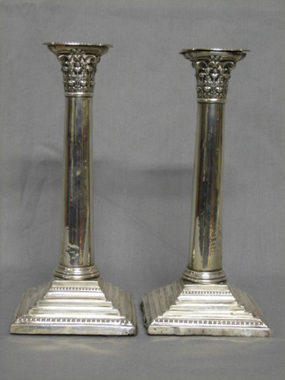 A pair of Edwardian silver candlesticks with Corinthian column capitals and detachable sconces, raised on square stepped feet, Sheffield 1914 9" (some holes and dents)