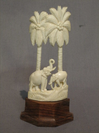 A carved ivory figure of 2 standing elephants beneath palm trees 5", raised on a hardwood base