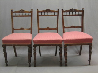 A set of 3 Edwardian walnut dining chairs with carved rail backs and bobbin decoration, raised on turned supports with upholstered seats