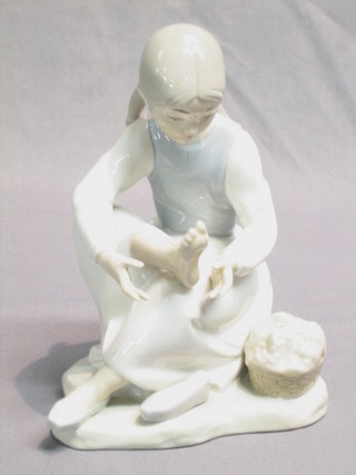 A Nao figure of a crouching girl examining her foot 8"