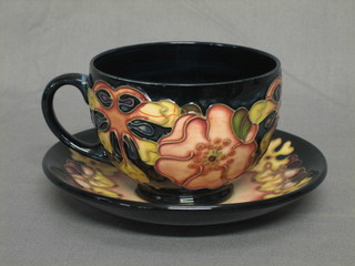 A Moorcroft Oberon pattern cup and saucer with floral decoration, cup signed M H (Marjore Hill) , saucer signed M H 1993 (slight chip to saucer)
