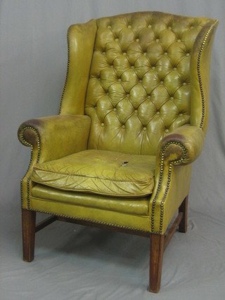 A Georgian style mahogany winged armchair upholstered in green buttoned leather