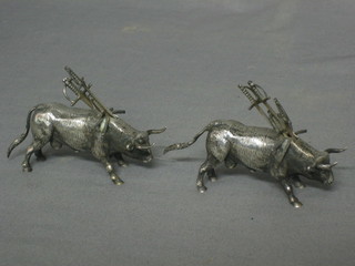 A pair of Eastern "silver" tooth pick holders in the form of bulls, both containing various tooth picks in the form of swords