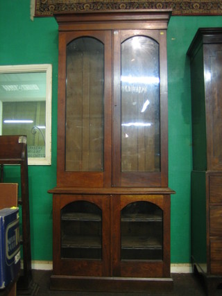 A Victorian oak bookcase on cabinet the upper section with moulded cornice, the interior fitted adjustable shelves enclosed by arch glazed panelled doors, the base fitted adjustable shelves enclosed by panelled doors, raised on a platform base 39"