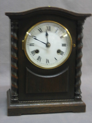 A striking bracket clock with enamelled dial and Roman numerals contained in an oak arch shaped case with spiral turned columns to the side