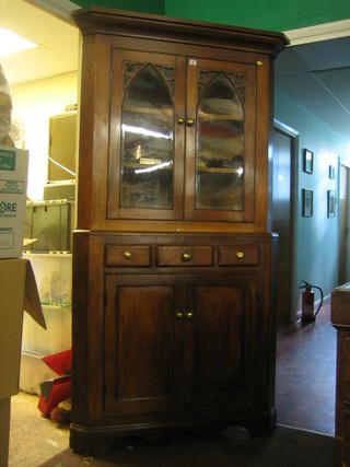 A Victorian Gothic oak double corner cabinet, with moulded cornice, the upper section fitted 3 shelves enclosed by arch plate glazed panelled doors, the base fitted 1 short drawer flanked by 2 dummy drawers above a double cupboard enclosed by a panelled door, raised on bracket feet 44"