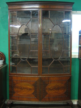  An Edwardian Georgian style mahogany bow front display cabinet with moulded and dentil cornice, the interior fitted adjustable shelves enclosed by astragal glazed panelled doors, the base fitted a cupboard enclosed by oval panelled doors, raised on carved cabriole claw and ball supports 51"