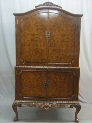 A 1950's Queen Anne style figured walnut cocktail cabinet with arched top, the upper section fitted a cupboard enclosed by a panelled door, the base fitted a double cupboard enclosed by a panelled door, raised on cabriole supports 37"