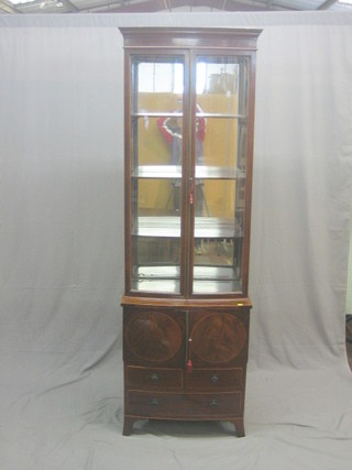 An Edwardian mahogany display cabinet with moulded cornice and mirrored back, fitted adjustable shelves enclosed by glazed panelled doors, raised on a George III mahogany bow front commode  converted for use as a cupboard enclosed by panelled door, the base fitted 2 short and 2 long drawers, raised on bracket feet 26"