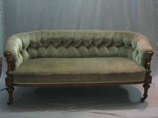 A Victorian walnut show frame sofa upholstered in green buttoned material, raised on fluted supports 62"