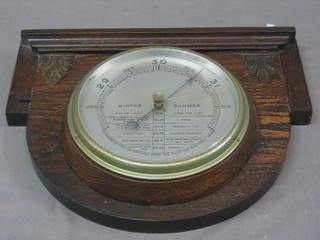 An aneroid barometer with silvered dial contained in a carved oak case