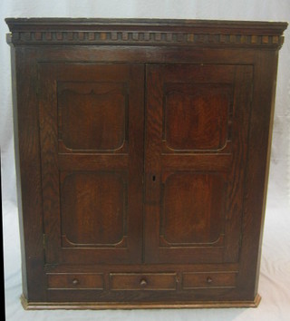 An 18th Century oak hanging corner cabinet with moulded and dentil cornice, the interior fitted shelves enclosed by panelled doors, the base fitted 1 long and 2 dummy drawers 35"