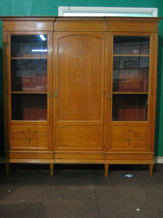 A handsome Edwardian inlaid satinwood triple bookcase with inlaid dentil cornice and swag, the central section enclosed by an inlaid panelled door flanked by a pair of cupboards enclosed by inlaid panelled doors, raised on square tapering supports ending in spade feet 69"