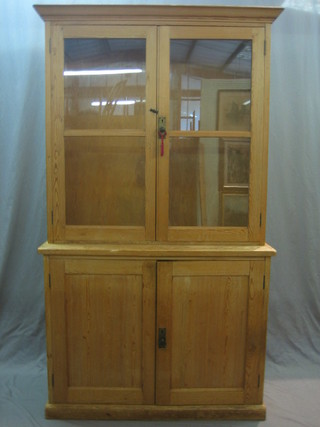 A pine bookcase on cabinet, the upper section with moulded cornice, the interior fitted adjustable shelves enclosed by glazed panelled doors, the base fitted a cupboard enclosed by a panelled door 44"