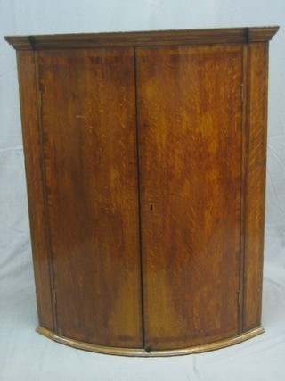 An 18th/19th Century oak bow front hanging corner cabinet with moulded cornice, fitted adjustable shelves enclosed by a pair of panelled doors, 33"