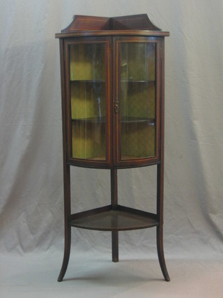An Edwardian inlaid mahogany bow front corner cabinet with raised back, the interior fitted shelves enclosed by glazed panelled doors with undertier raised on outswept supports 21"