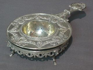 An embossed white metal tea strainer and stand