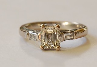 A lady's 18ct white gold dress ring set a rectangular emerald cut diamond supported by 2 baguette diamonds to the shoulders, centre stone approx 0.85ct