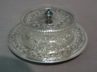 A circular moulded glass butter dish contained in a Britannia metal stand