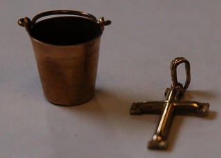 A gold charm in the form of a cross and 1 other in the form of a bucket