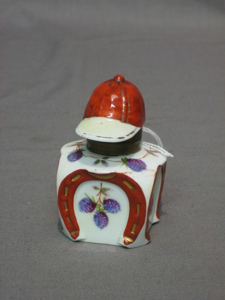 A Continental porcelain inkwell, the hinged lid in the form of a jockey's cap, the base decorated horse shoes 3"