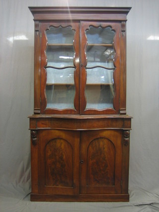 A Victorian mahogany bookcase on cabinet the upper section with moulded cornice fitted adjustable shelves enclosed by glazed panelled doors, the base of serpentine outline fitted a drawer above a pair of arch shaped panelled doors and raised on a platform base 43"