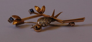 A 9ct gold bar brooch in the form of a bird sat on a branch, set diamonds and a sapphire