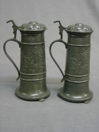 A pair of Continental embossed pewter steins with hinged lids, raised on 3 bun feet (dented) 9"