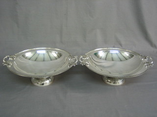 A pair of circular silver plated twin handled bowls, raised on spreading feet 12"