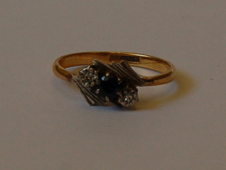 A gold dress ring set a blue coloured stone supported by 2 illusion set diamonds