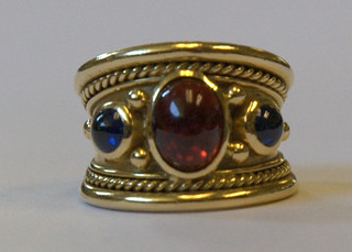 An 18ct gold dress ring set a cabouchon cut red stone supported by 2 cabouchon cut blue stones