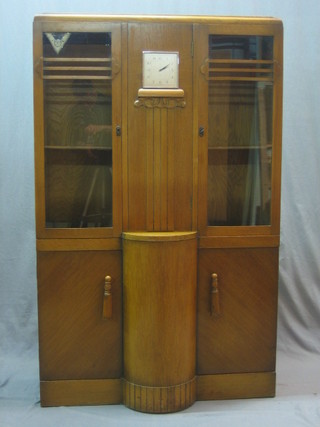 An Art Deco honey oak display cabinet, the centre section fitted an 8 day timepiece and having a secret letter compartment flanked by a pair of cupboards fitted shelves and enclosed by astragal glazed doors, the base fitted 2 cupboards enclosed by panelled doors 36"