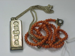 A silver ingot pendant hung on a silver chain and a string on coral beads