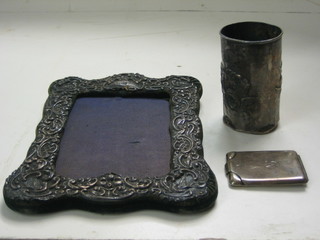 An Edwardian embossed silver easel photograph frame (f) 8", a silver match slip and a silver bottle holder (f)