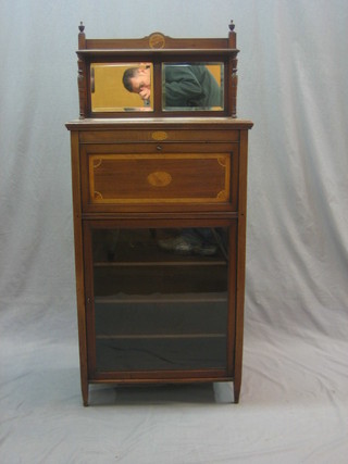 An Edwardian inlaid mahogany music cabinet with raised mirrored back, having a fall front above a glazed panelled door, the interior fitted adjustable shelves
